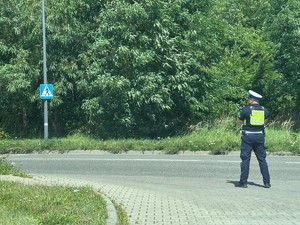 Zdjęcie przedstawia umundurowanego policjanta z wydziału ruchu drogowego podczas czynności.