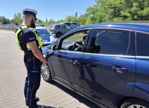 Zdjęcie przedstawia umundurowanego policjanta z wydziału ruchu drogowego podczas czynności.