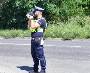 Zdjęcie przedstawia umundurowanego policjanta z wydziału ruchu drogowego podczas czynności.