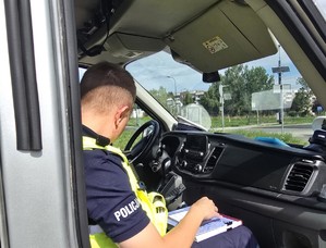Zdjęcie przedstawia umundurowanego policjanta z wydziału ruchu drogowego podczas czynności.