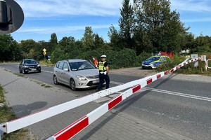 Zdjęcie przedstawia umundurowanego policjanta oraz przedstawicieli w rejonie przejazdu kolejowego.