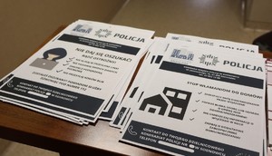 Zdjęcie przedstawia ulotki profilaktyczne leżące na stole. Ulotki dotyczą włamań do mieszkań oraz oszustw.