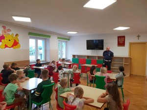 Zdjęcie przedstawia umundurowanego policjanta prowadzącego pogadankę z grupą dzieci.