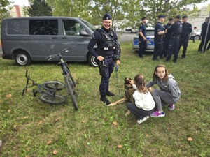 Zdjęcie przedstawia umundurowanego policjanta, psa służbowego oraz dzieci podczas pikniku.