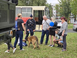 Zdjęcie przedstawia umundurowanego policjanta, psa służbowego oraz dzieci podczas pikniku.