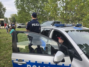 Zdjęcie przedstawia umundurowanego policjanta oraz dziecko przy oznakowanym radiowozie.