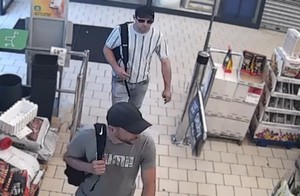 Zdjęcie przedstawia dwóch mężczyzn w czarnych czapkach z daszkiem na terenie sklepu.