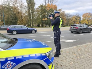 Zdjęcie przedstawia umundurowanego policjanta Wydziału Ruchu Drogowego podczas czynności służbowych.