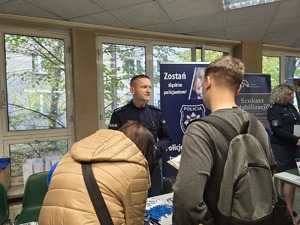 Zdjęcie przedstawia umundurowanego policjanta rozmawiającego z uczestnikami wydarzenia.