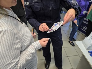 Zdjęcie przedstawia umundurowanych policjantów oraz uczestników. W tle ulotki zachęcające do służby w Policji.