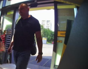Zdjęcie przedstawia mężczyznę w czarnym T-shircie i spodniach jeansowych na terenie sklepu.