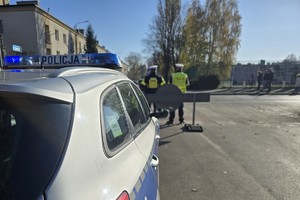 Zdjęcie przedstawia oznakowany radiowóz policyjny oraz dwóch, umundurowanych policjantów.