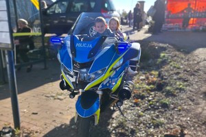 Zdjęcie przedstawia dwoje dzieci na motocyklu służbowym.
