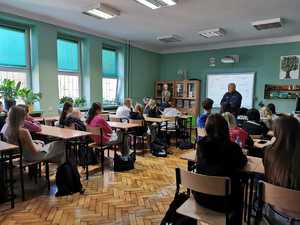 Zdjęcie przedstawia umundurowanego policjanta prowadzącego prelekcję w szkole.