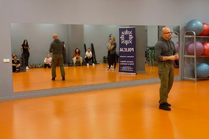 Zdjęcie przedstawia instruktora policyjnego prowadzącego zajęcia dla uczestniczek kursu w sali.