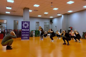 Zdjęcie przedstawia instruktora policyjnego prowadzącego zajęcia dla uczestniczek kursu w sali.