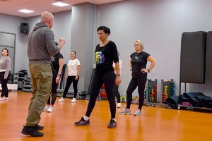 Zdjęcie przedstawia instruktora policyjnego prowadzącego zajęcia dla uczestniczek kursu w sali.