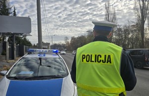 Zdjęcie przedstawia umundurowanego policjanta oraz radiowóz podczas działań.
