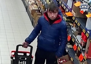 Zdjęcie przedstawia mężczyznę w niebieskiej kurtce na terenie sklepu.