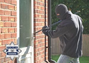 Zdjęcie przedstawia zamaskowaną osobę próbującą włamać się do domu.