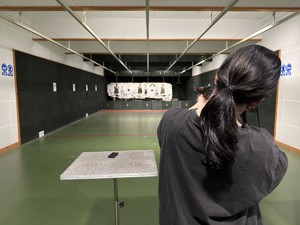 Zdjęcie przedstawia kobietę z bronią na terenie strzelnicy.