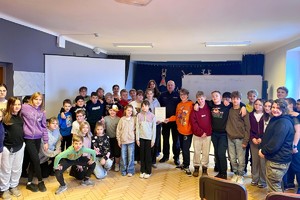 Zdjęcie przedstawia umundurowanego policjanta z grupą dzieci pozujących do zdjęcia w sali.