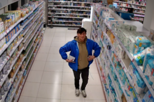 Zdjęcie przedstawia mężczyznę w niebieskiej kurtce na terenie sklepu.