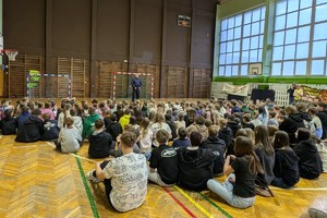 Zdjęcie przedstawia policjanta prowadzącego prelekcję w sali gimnastycznej.