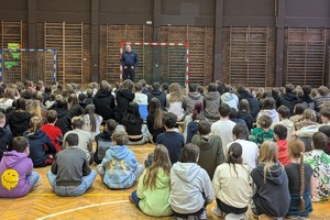 Zdjęcie przedstawia policjanta prowadzącego prelekcję w sali gimnastycznej.