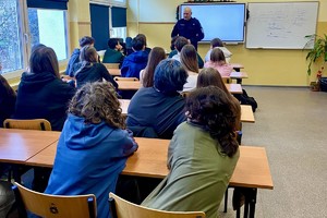 Zdjęcie przedstawia umundurowanego policjanta w sali z uczniami.