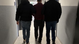 Zdjęcie przedstawia dwóch nieumundurowanych policjantów oraz zatrzymanego mężczyznę.
