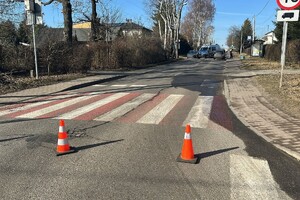 Zdjęcie przedstawia oznakowane przejście dla pieszych. W tle samochody, oznakowany radiowóz oraz umundurowany policjant.