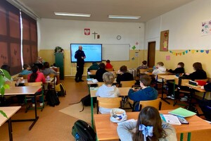 Zdjęcie przedstawia umundurowanego policjanta w sali lekcyjnej z uczniami.