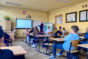 Zdjęcie przedstawia umundurowanego policjanta podczas prelekcji w sali lekcyjnej.