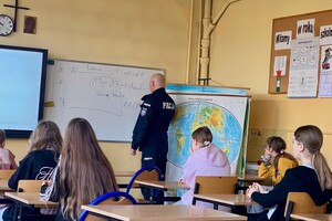 Zdjęcie przedstawia umundurowanego policjanta podczas prelekcji w sali lekcyjnej.