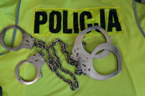 Zdjęcie przedstawia policyjną kamizelkę oraz kajdanki zespolone