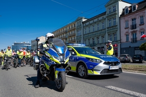 Zdjęcie przedstawia umundurowanego policjanta na motocyklu oraz oznakowany radiowóz.