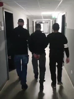 Na zdjęciu widać dwóch nieumundurowanych policjantów prowadzących zatrzymanego mężczyznę.