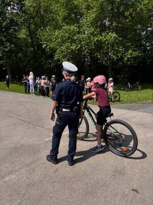Zdjęcie przedstawia umundurowaną policjantkę wraz z dzieckiem na rowerze