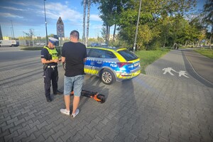 Zdjęcie przedstawia umundurowanego policjanta kontrolującego kierującego hulajnogą elektryczną.