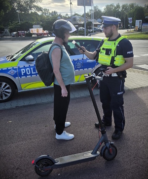 Zdjęcie przedstawia umundurowanego policjanta kontrolującego kierującego hulajnogą elektryczną.