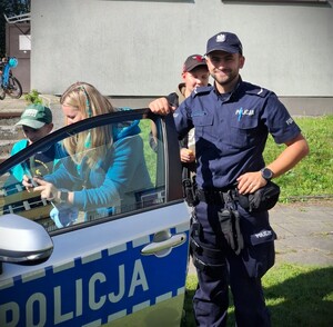 Policjant przy radiowozie z dziećmi.