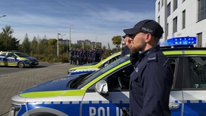 Policjanci podczas oddawania honoru. Oznakowane radiowozy.
