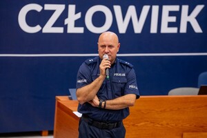 Umundurowany policjant przemawiający do gości.