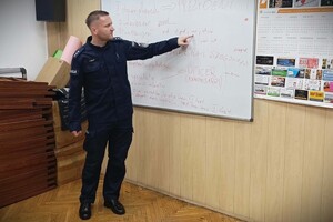 Umundurowany policjant podczas zajęć przy tablicy.