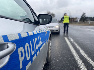 Umundurowana policjantka podczas kontroli trzeźwości. Oznakowany radiowóz służbowy.